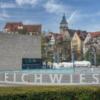 Stadtansicht von Backnang mit modernen und historischen Gebäuden, im Vordergrund der Schriftzug 'Bleichwiese' und ein Platz mit geschlossenen Sonnenschirmen., © René Straube