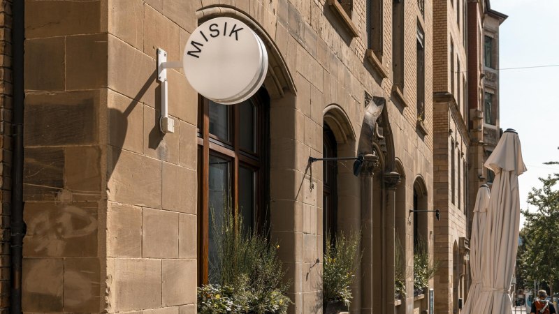 Gebäude mit Sandsteinfassade, rundes Schild mit 'MISIK', Fenster mit Pflanzen, geschlossene Sonnenschirme auf der Straße., © Stuttgart-Marketing GmbH, Sarah Schmid Gebäude mit Sandsteinfassade, rundes Schild mit 'MISIK', Fenster mit Pflanzen, geschlossene Sonnenschirme auf der Straße., © Stuttgart-Marketing GmbH, Sarah Schmid