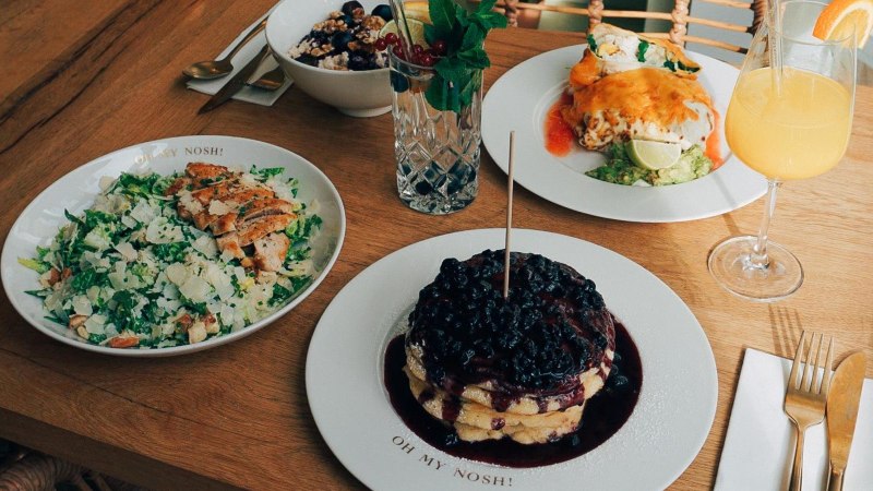 Ein Tisch mit Salat, Pfannkuchen mit Beeren, einem Getränk und weiteren Speisen auf Holztisch., © The Gardeners Nosh, Stuttgart Ein Tisch mit Salat, Pfannkuchen mit Beeren, einem Getränk und weiteren Speisen auf Holztisch., © The Gardeners Nosh, Stuttgart