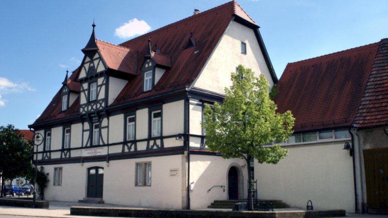 Fachwerkhaus mit rotem Satteldach und dekorativen Giebeln. Ein Baum steht im Vordergrund, der Himmel ist blau mit wenigen Wolken., © Nürtingen - Stuttgart-Marketing GmbH Fachwerkhaus mit rotem Satteldach und dekorativen Giebeln. Ein Baum steht im Vordergrund, der Himmel ist blau mit wenigen Wolken., © Nürtingen - Stuttgart-Marketing GmbH