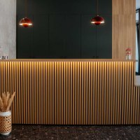 Ein stilvoller Empfangsbereich mit einer Holztheke, dekorativen Lampen und Broschürenregalen an der Wand., © Nik Ebert Ein stilvoller Empfangsbereich mit einer Holztheke, dekorativen Lampen und Broschürenregalen an der Wand., © Nik Ebert