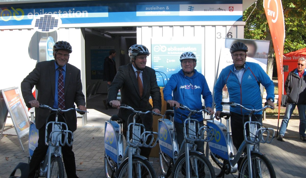 Vier Männer mit Helmen posieren vor einer E-Bike-Station in Holzgerlingen. Sie halten E-Bikes und lächeln in die Kamera., © Natur.Nah. Schönbuch & Heckengäu Vier Männer mit Helmen posieren vor einer E-Bike-Station in Holzgerlingen. Sie halten E-Bikes und lächeln in die Kamera., © Natur.Nah. Schönbuch & Heckengäu