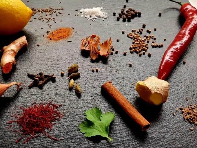 Eine Auswahl an Gewürzen und Zutaten, darunter Zitrone, Chili, Ingwer, Zimt, Kardamom und Safran, auf einer dunklen Oberfläche arrangiert., © Kultweine-Kochwelten-Kunstücke - Kochschule Sonja Lenz Eine Auswahl an Gewürzen und Zutaten, darunter Zitrone, Chili, Ingwer, Zimt, Kardamom und Safran, auf einer dunklen Oberfläche arrangiert., © Kultweine-Kochwelten-Kunstücke - Kochschule Sonja Lenz