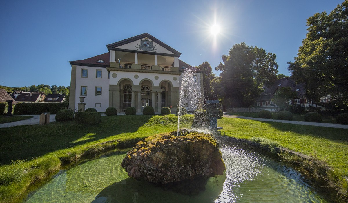 Schloss Dätzingen mit einem Springbrunnen im Vordergrund. Die Sonne scheint hell am blauen Himmel, umgeben von grünen Bäumen und gepflegtem Rasen., © Stuttgart Marketing GmbH Schloss Dätzingen mit einem Springbrunnen im Vordergrund. Die Sonne scheint hell am blauen Himmel, umgeben von grünen Bäumen und gepflegtem Rasen., © Stuttgart Marketing GmbH