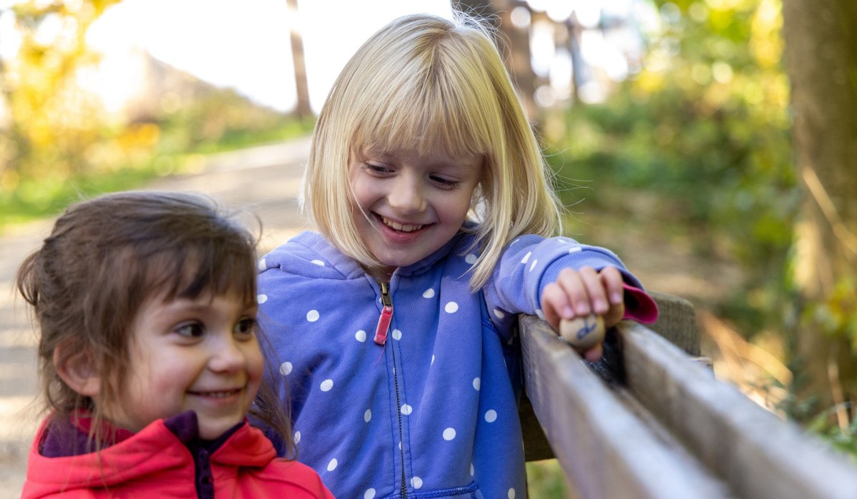 Zwei lachende Kinder spielen an einer Holzkugelbahn im Wald. Eines der Kinder hält eine Kugel in der Hand., © Thomas Zehnder