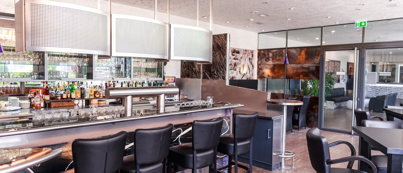 Moderne Bar mit schwarzen Hockern, glänzender Theke und gut bestücktem Regal. Helle Decke mit Beleuchtung, stilvolle Einrichtung., © Plaza Residence Stuttgart-Ditzingen Moderne Bar mit schwarzen Hockern, glänzender Theke und gut bestücktem Regal. Helle Decke mit Beleuchtung, stilvolle Einrichtung., © Plaza Residence Stuttgart-Ditzingen