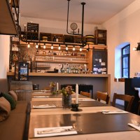 Gem&uuml;tliches Restaurant mit Bar, Holztischen und -st&uuml;hlen, dekorativen Elementen und warmem Licht. Die Bar ist gut best&uuml;ckt mit Flaschen und Gl&auml;sern.