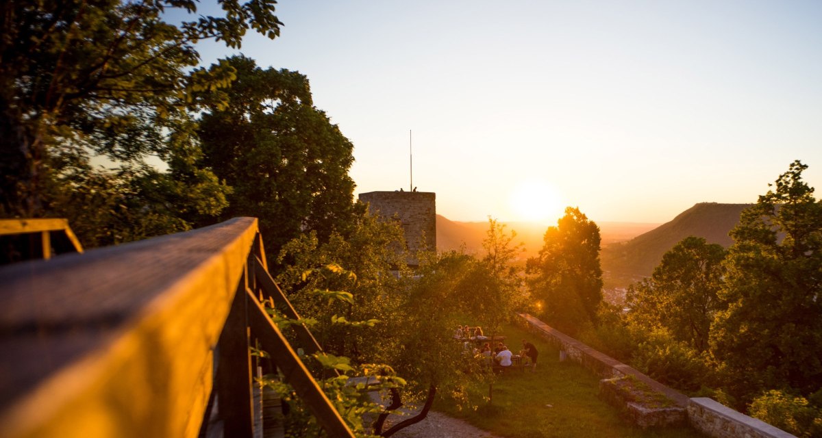 Die Burgruine Helfenstein bei Sonnenuntergang, umgeben von B&auml;umen. Menschen sitzen auf einer Wiese und genie&szlig;en die Aussicht., &copy; Landkreis G&ouml;ppingen