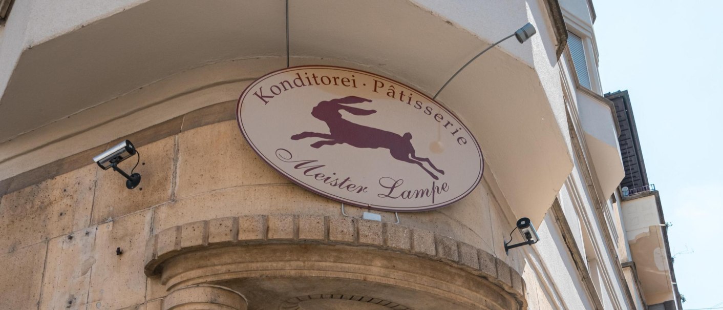 Schild der Konditorei 'Meister Lampe' mit springendem Hasen, an einer Gebäudefassade montiert., © SMG, Sarah Schmid Schild der Konditorei 'Meister Lampe' mit springendem Hasen, an einer Gebäudefassade montiert., © SMG, Sarah Schmid