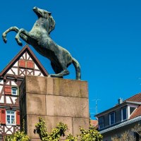 Eine Pferdestatue auf einem Sockel vor traditionellen Fachwerkhäusern in Kirchheim unter Teck, unter klarem, blauem Himmel., © Stuttgart-Marketing GmbH, Sarah Schmid Eine Pferdestatue auf einem Sockel vor traditionellen Fachwerkhäusern in Kirchheim unter Teck, unter klarem, blauem Himmel., © Stuttgart-Marketing GmbH, Sarah Schmid