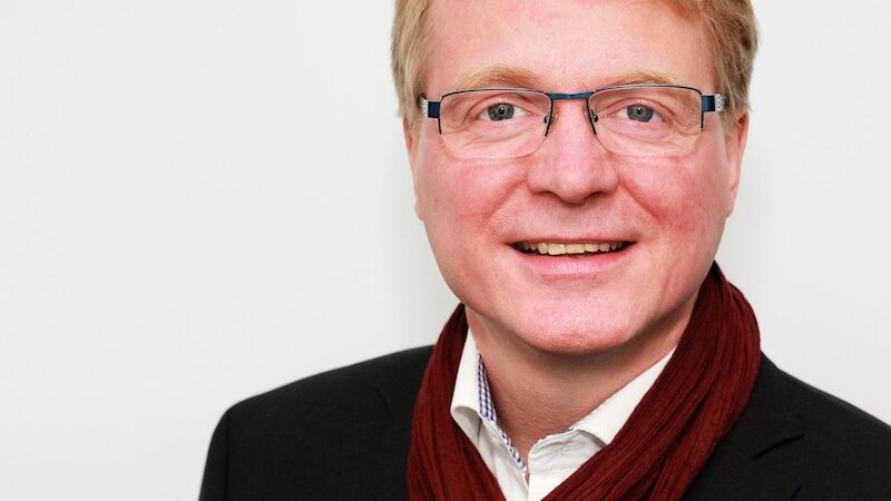 Ein Mann mit Brille und rotem Schal l&auml;chelt in die Kamera. Er tr&auml;gt einen dunklen Anzug und steht vor einem wei&szlig;en Hintergrund., &copy; Sch&ouml;nblick gemeinn&uuml;tzige GmbH