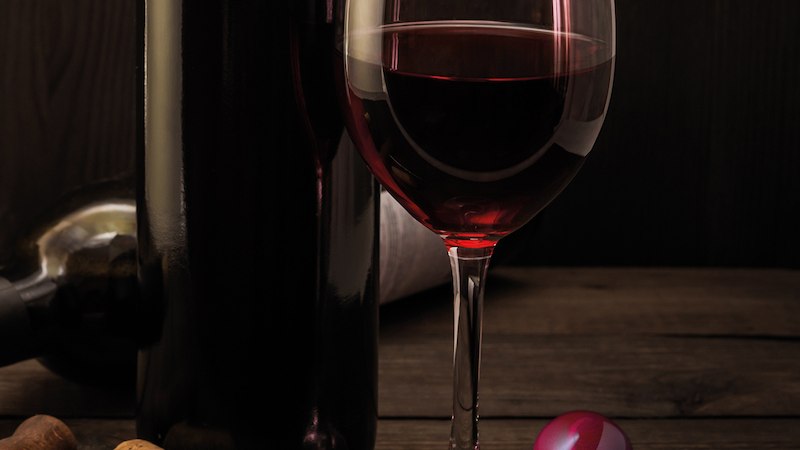 Ein Glas Rotwein steht neben einer Weinflasche auf einem Holztisch. Ein Korkenzieher und ein rosa Schokoladenbonbon liegen daneben., © Mercedes-Benz AG Ein Glas Rotwein steht neben einer Weinflasche auf einem Holztisch. Ein Korkenzieher und ein rosa Schokoladenbonbon liegen daneben., © Mercedes-Benz AG