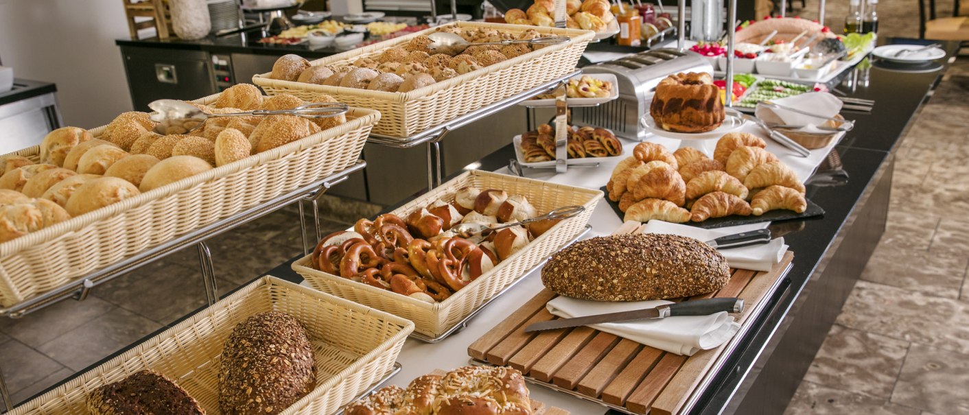 Ein Frühstücksbuffet mit einer Auswahl an Broten, Gebäck, Croissants und Säften auf einem Tisch., © ARCOTEL Hotels