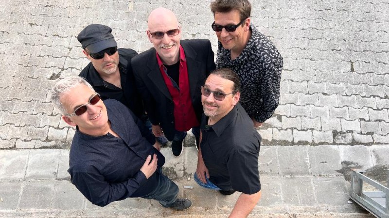 Fünf Männer in schwarzer Kleidung stehen auf einem gepflasterten Boden und blicken lächelnd nach oben in die Kamera., © Foto Fridge People Fünf Männer in schwarzer Kleidung stehen auf einem gepflasterten Boden und blicken lächelnd nach oben in die Kamera., © Foto Fridge People