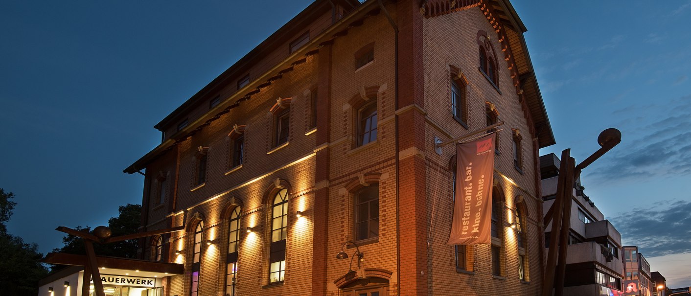 Das Mauerwerk in Herrenberg bei Dämmerung, ein beleuchtetes Backsteingebäude mit großen Fenstern und einem Banner. Der Himmel ist dunkelblau., © Stadt Herrenberg Das Mauerwerk in Herrenberg bei Dämmerung, ein beleuchtetes Backsteingebäude mit großen Fenstern und einem Banner. Der Himmel ist dunkelblau., © Stadt Herrenberg