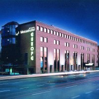 Beleuchtetes Messehotel Europe bei Nacht, mit leuchtendem Schriftzug und vorbeifahrenden Autos auf der Straße., © Messehotel Europe
