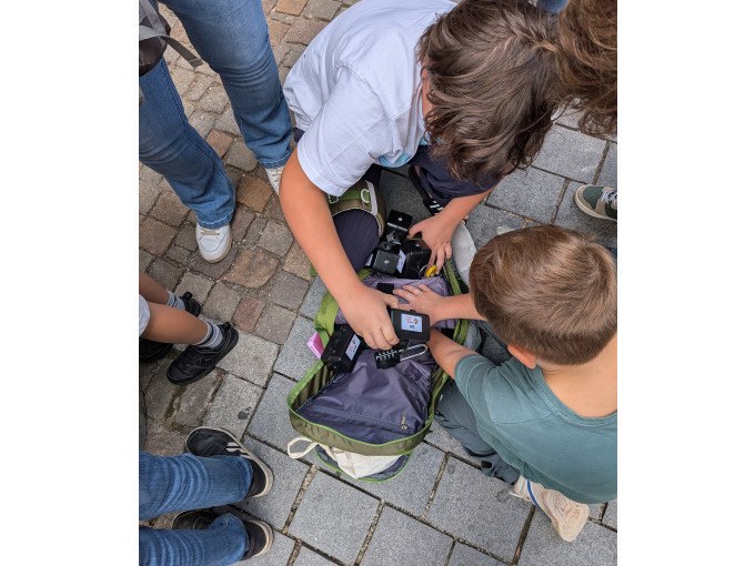 Kinder beugen sich &uuml;ber einen Rucksack mit technischen Ger&auml;ten auf einer gepflasterten Stra&szlig;e., &copy; Eigenbetrieb Tourismus und Citymanagement Schorndorf