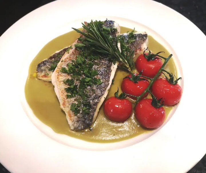 Ein Fischgericht auf grünem Püree, garniert mit frischen Kräutern und Kirschtomaten auf einem weißen Teller., © La buona Forketta Ein Fischgericht auf grünem Püree, garniert mit frischen Kräutern und Kirschtomaten auf einem weißen Teller., © La buona Forketta