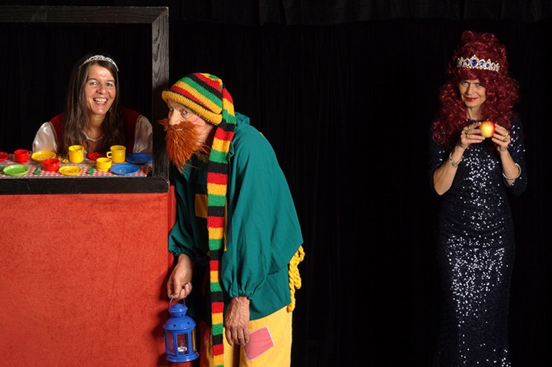 Drei Personen in Kostümen: eine Frau in einem Puppentheater, ein Mann als Zwerg und eine Frau mit Krone und Apfel., © Galli Theater Backnang