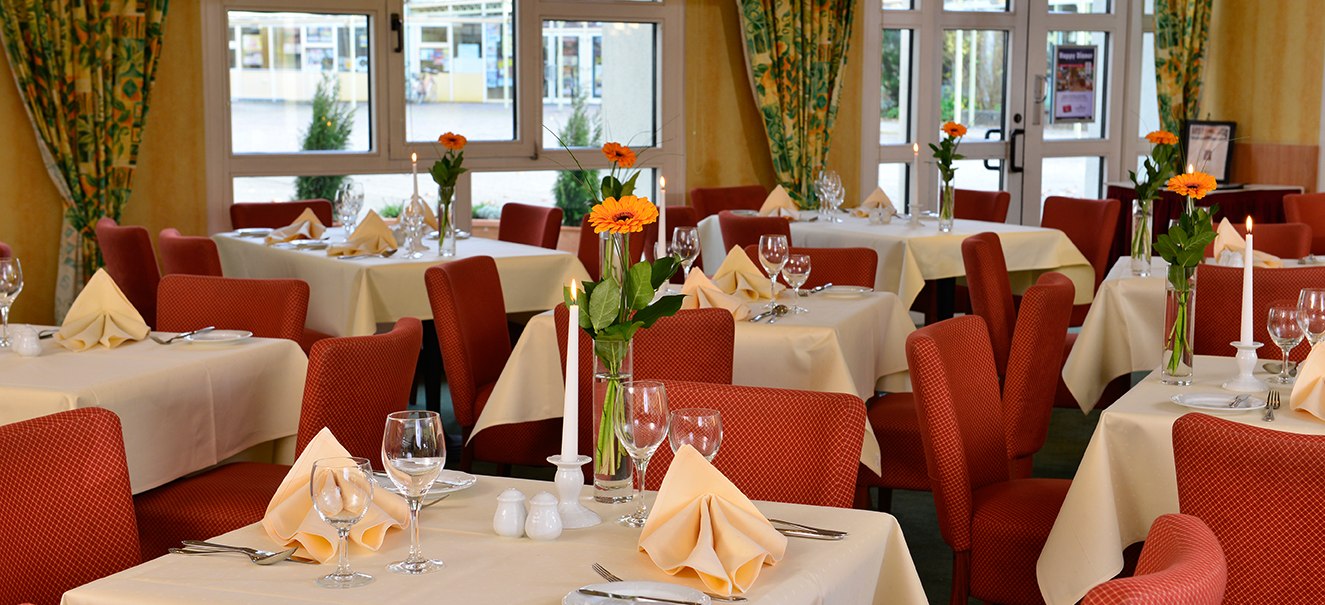 Elegantes Restaurant mit roten St&uuml;hlen, wei&szlig;en Tischdecken und Blumen auf den Tischen. Gro&szlig;e Fenster im Hintergrund., &copy; Amber Hotel Leonberg / Stuttgart
