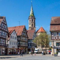 Fachwerkhäuser am Marktplatz in Schorndorf, mit einem Kirchturm im Hintergrund. Menschen spazieren über den Platz bei sonnigem Wetter., © Stuttgart-Marketing GmbH