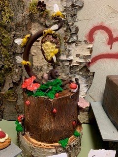 Ein kunstvoll dekorierter Kuchen in Form eines Baumstamms mit Bienen, Pilzen und Moos. Im Hintergrund ist eine Birkenrinde und ein rotes Herz zu sehen., &copy; Cafe Brunenberg