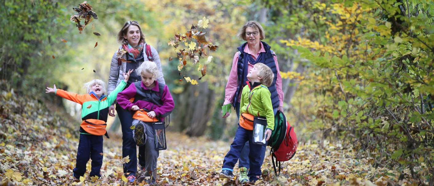 Familie auf einem Waldweg im Herbst, Kinder werfen Laub in die Luft. Bunte Blätter und fröhliche Gesichter in einer herbstlichen Umgebung., © Bad Urach Tourismus