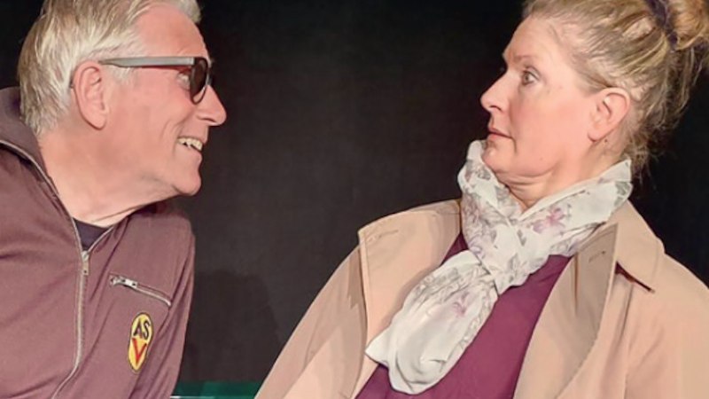 Ein Mann mit Sonnenbrille lächelt eine Frau an, die überrascht wirkt. Beide stehen auf einer Bühne, die Frau trägt einen Schal., © Theaterwerkstatt Schwäbisch Gmünd e.V.