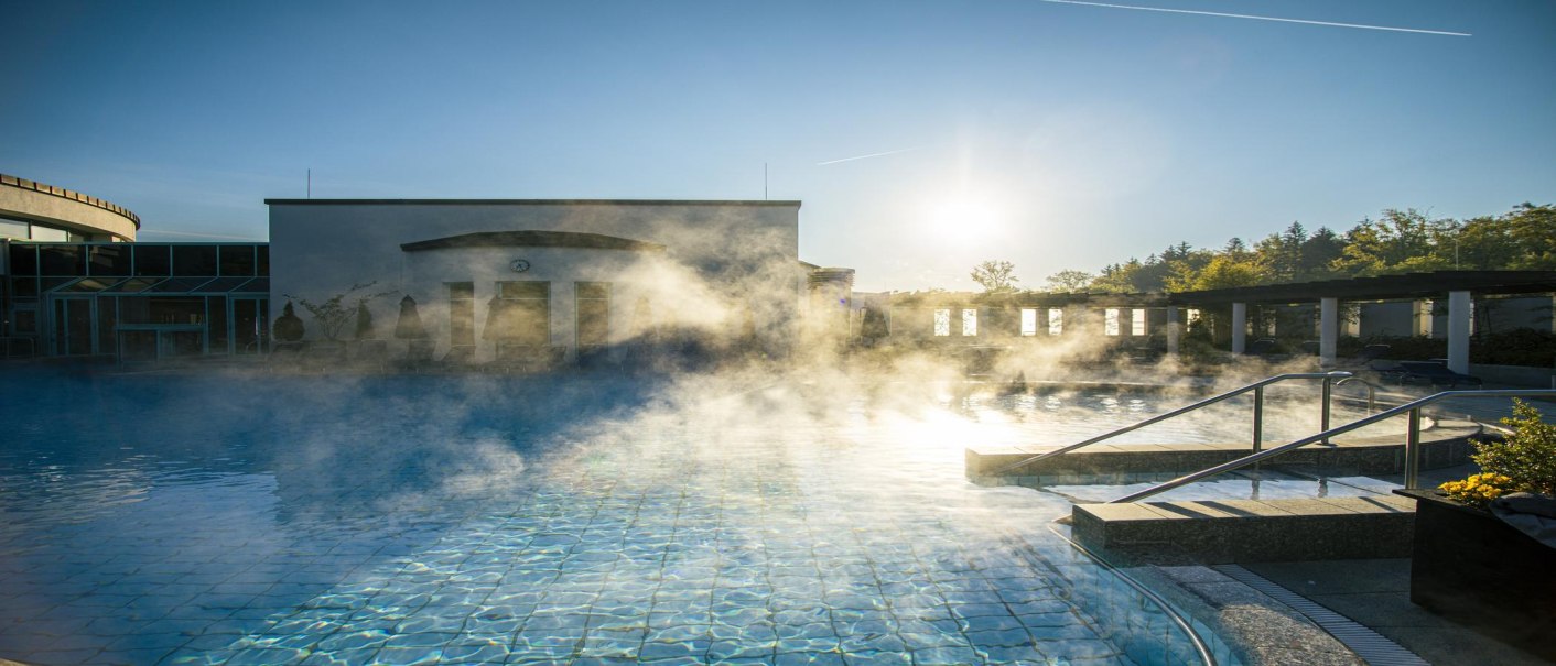 Dampf steigt aus dem Außenpool der Böblingen Mineraltherme auf, während die Sonne am klaren Himmel scheint., © SMG, Sarah Schmid