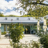 Eingang der Vinzenz Therme in Bad Ditzenbach, umgeben von üppigem Grün und einem sonnigen Himmel., © SMG, Sarah Schmid Eingang der Vinzenz Therme in Bad Ditzenbach, umgeben von üppigem Grün und einem sonnigen Himmel., © SMG, Sarah Schmid