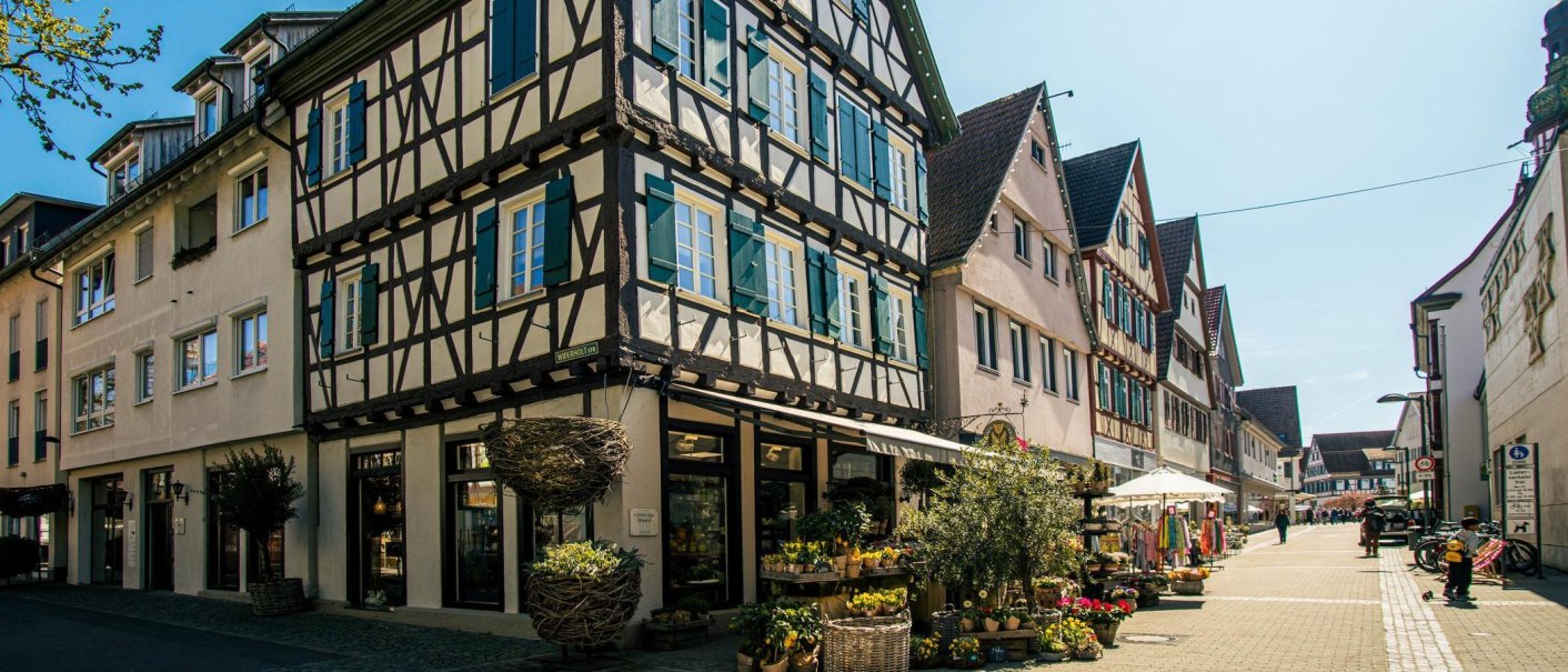 Fachwerkhäuser in der Altstadt von Kirchheim unter Teck. Die Straße ist belebt mit Geschäften und Fußgängern. Blumen und Dekorationen schmücken die Szene., © Stuttgart-Marketing GmbH, Sarah Schmid