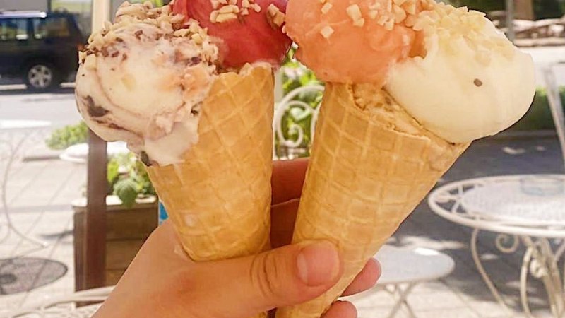 Drei Eiswaffeln mit verschiedenen Eissorten und N&uuml;ssen, gehalten von einer Hand unter einem Sonnenschirm im Freien., &copy; E. Dogan