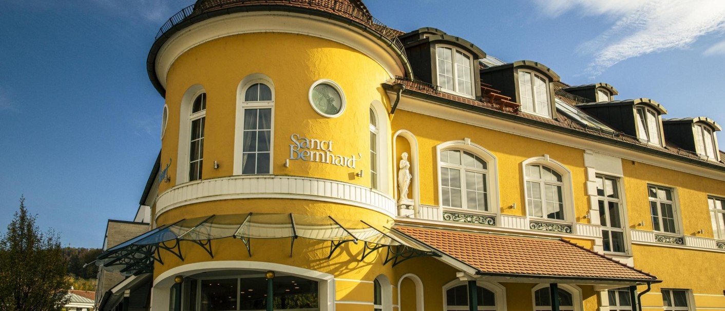 Gelbes Gebäude mit Rundturm und Schriftzug 'Sanct Bernhard'. Der Himmel ist blau und klar., © SMG, Sarah Schmid