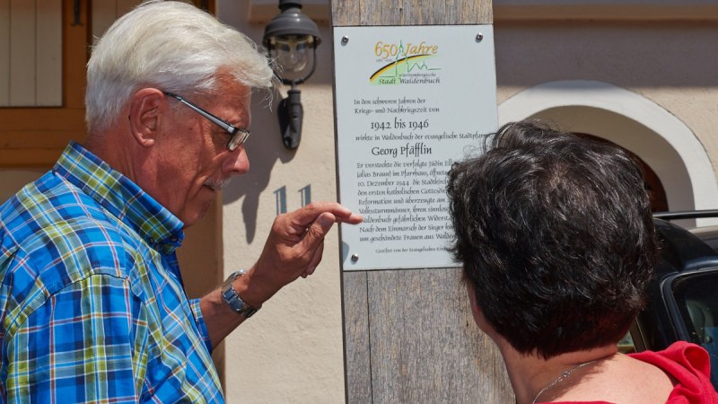Zwei Personen lesen eine Gedenktafel an einem Holzpfosten. Die Tafel erinnert an historische Ereignisse in der Stadt Waldenbuch., © Natur.Nah. Schönbuch & Heckengäu Zwei Personen lesen eine Gedenktafel an einem Holzpfosten. Die Tafel erinnert an historische Ereignisse in der Stadt Waldenbuch., © Natur.Nah. Schönbuch & Heckengäu