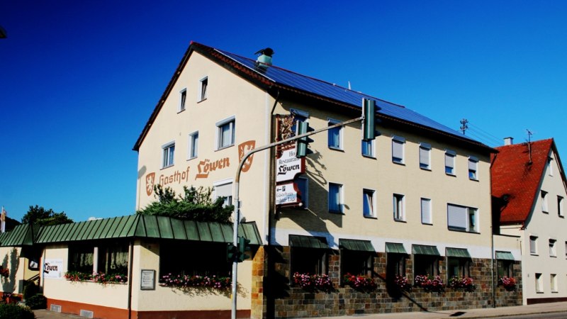 Der Gasthof Löwen mit beiger Fassade und roten Dächern, dekoriert mit Blumen, unter blauem Himmel., © Ulli Kellenbenz