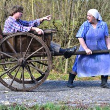 Eine Frau in Sch&uuml;rze zieht einen Mann in einem Holzkarren auf einem Waldweg. Beide sind in l&auml;ndlicher Kleidung gekleidet., &copy; links im Bild