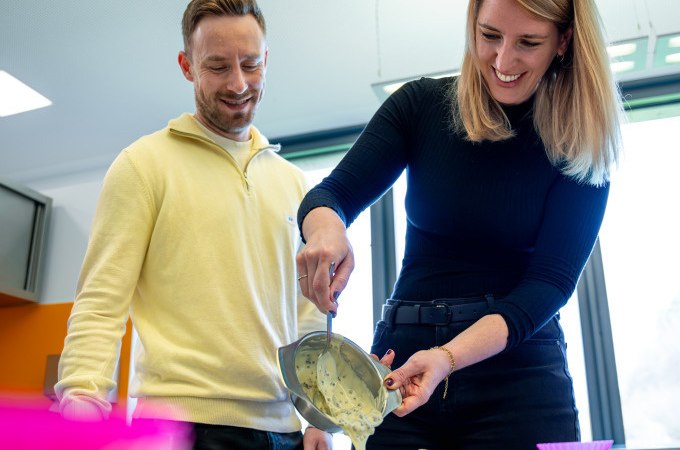 Zwei Personen gießen Schokoladenmasse in eine Form. Sie lächeln und arbeiten zusammen in einer hellen Umgebung., © Alfred Ritter GmbH &amp; Co. KG | Waldenbuch