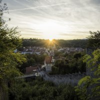 Sonnenuntergang über Schwäbisch Hall, gesehen von einer erhöhten Position mit Bäumen und alten Mauern im Vordergrund., © Patrick Krol