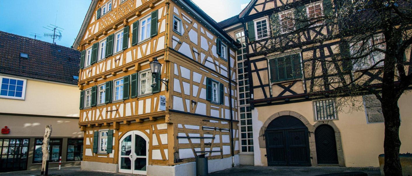 Fachwerkgebäude in Schorndorf mit grünen Fensterläden. Ein Baum steht im Vordergrund, daneben ein modernes Gebäude., © Stuttgart-Marketing GmbH, Sarah Schmid