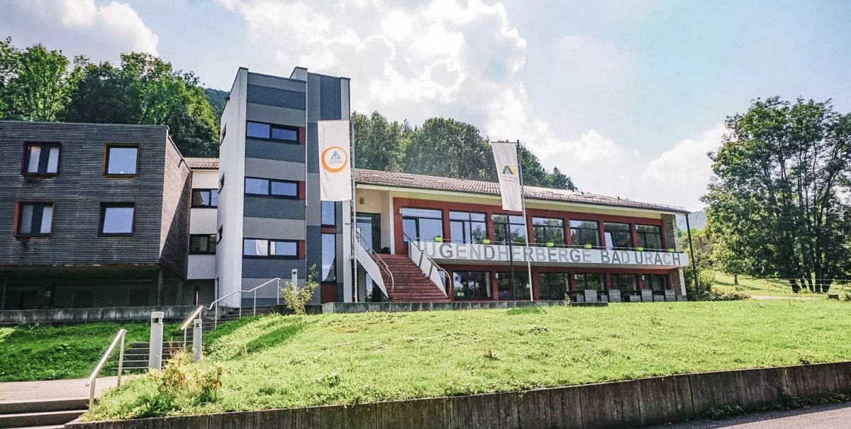 Die Jugendherberge Bad Urach liegt inmitten gr&uuml;ner Natur. Das moderne Geb&auml;ude hat gro&szlig;e Fenster und ist von B&auml;umen umgeben.