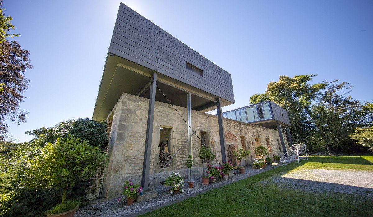Modernes Gebäude mit alten Steinmauern und Glasstruktur, umgeben von Pflanzen und Bäumen unter blauem Himmel., © Region Stuttgart