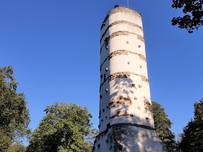 Ein runder Turm mit Klettergriffen, umgeben von B&auml;umen, unter klarem blauem Himmel., &copy; SwabianTravel