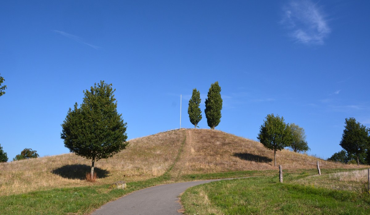Ein Hügel mit einem Pfad führt zu drei Bäumen und einem Fahnenmast. Der Himmel ist klar und blau., © Remstal Tourismus e.V.