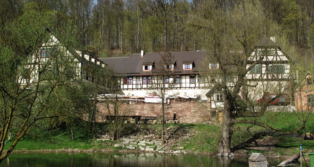 Ein malerisches Fachwerkhaus am Waldrand, umgeben von Bäumen. Im Vordergrund befindet sich ein kleiner Teich mit grünem Ufer., © RadL Leonberg Ein malerisches Fachwerkhaus am Waldrand, umgeben von Bäumen. Im Vordergrund befindet sich ein kleiner Teich mit grünem Ufer., © RadL Leonberg