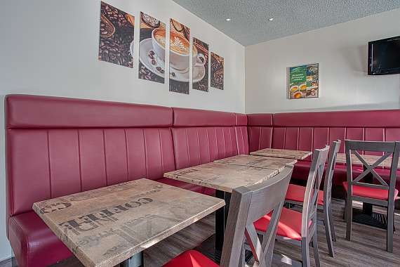 Frühstücksraum mit roten Sitzbänken, Holztischen und Stühlen. An der Wand hängen Kaffeebilder und ein Fernseher., © Centro Hotels