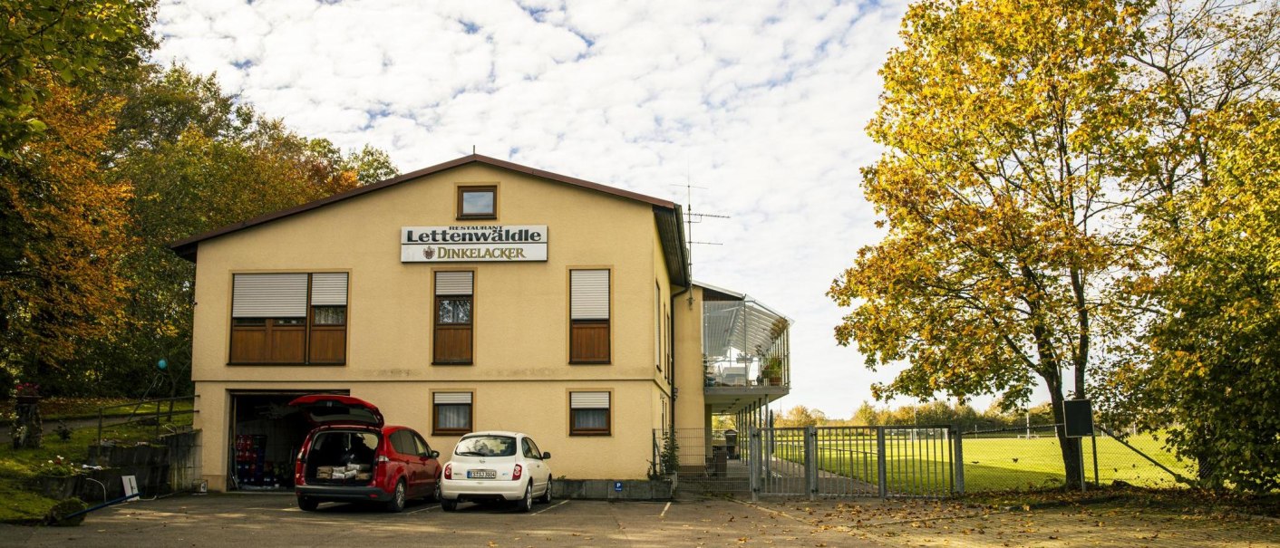Sportheim Lettenwäldle mit geparkten Autos, umgeben von herbstlichen Bäumen und einem Sportplatz im Hintergrund., © Stuttgart Marketing GmbH, Sarah Schmid