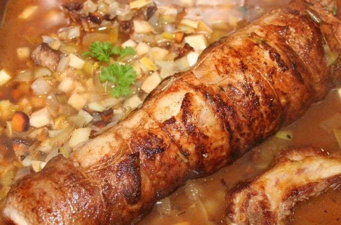 Ein gerollter Braten in einer Pfanne, umgeben von Gemüsewürfeln und einer braunen Sauce, garniert mit einem Petersilienzweig., © Kultweine-Kochwelten-Kunstücke - Kochschule Sonja Lenz Ein gerollter Braten in einer Pfanne, umgeben von Gemüsewürfeln und einer braunen Sauce, garniert mit einem Petersilienzweig., © Kultweine-Kochwelten-Kunstücke - Kochschule Sonja Lenz