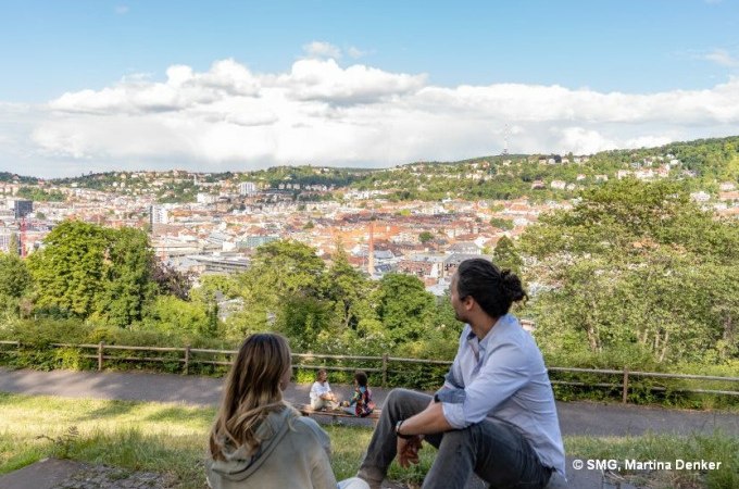 Zwei Personen sitzen auf einer Bank und genie&szlig;en den Ausblick auf Stuttgart. Im Hintergrund sind gr&uuml;ne H&uuml;gel und die Stadtlandschaft zu sehen., &copy; Stuttgart Marketing GmbH