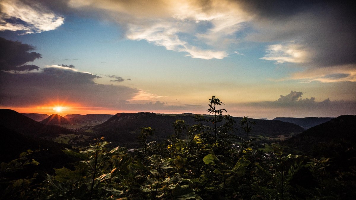 Sonnenuntergang über einer hügeligen Landschaft, Pflanzen im Vordergrund. Der Himmel zeigt ein Farbspiel aus Orange, Blau und Wolken., © Landkreis Göppingen Sonnenuntergang über einer hügeligen Landschaft, Pflanzen im Vordergrund. Der Himmel zeigt ein Farbspiel aus Orange, Blau und Wolken., © Landkreis Göppingen