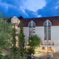 Das Best Western Plus Hotel am Schlossberg bei Dämmerung, mit beleuchteten Fenstern und einem gläsernen Treppenhaus, umgeben von Bäumen., © Best Western Plus Hotel am Schlossberg